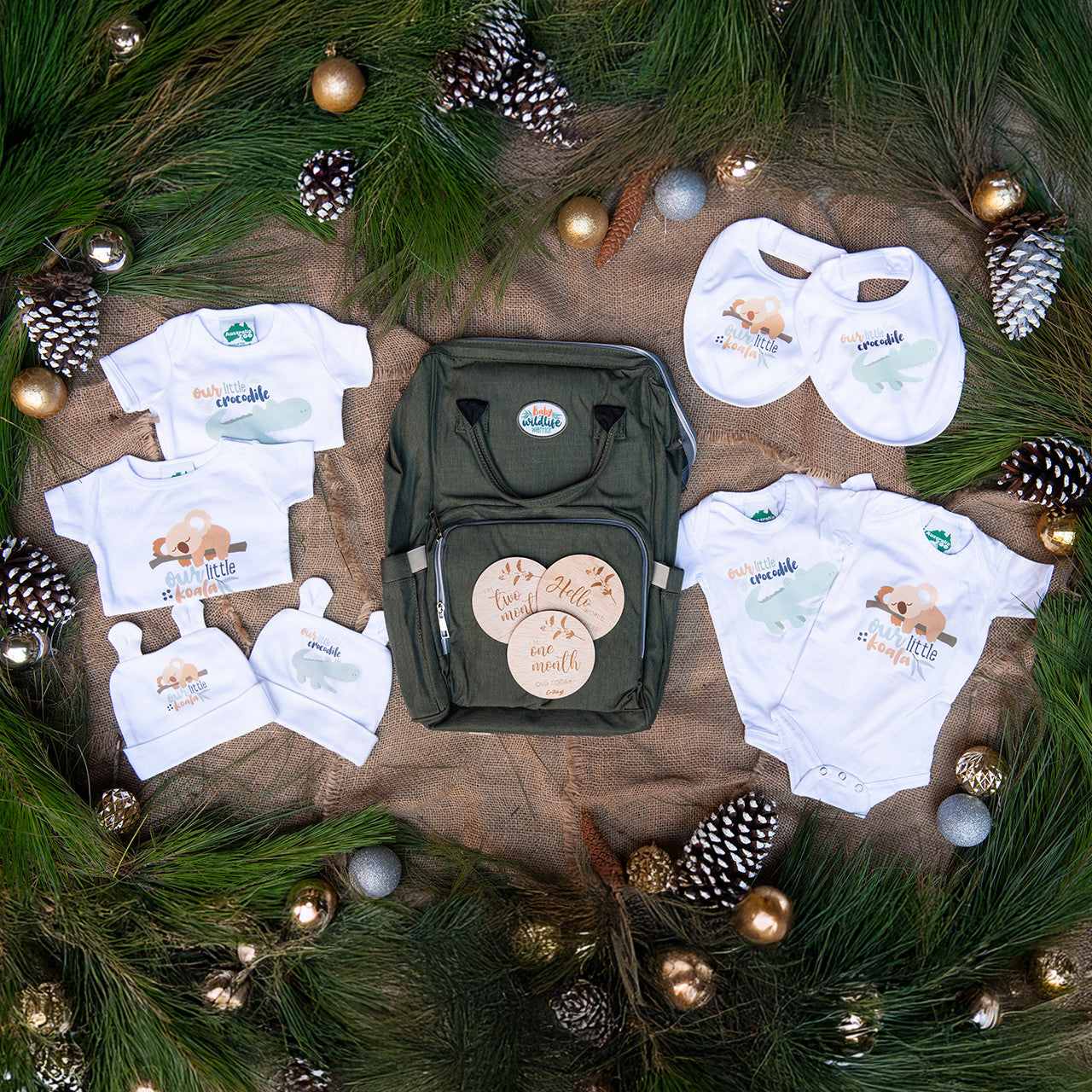 Australia Zoo baby clothing and diaper bag set on a decorative Christmas background with pine branches and ornaments.