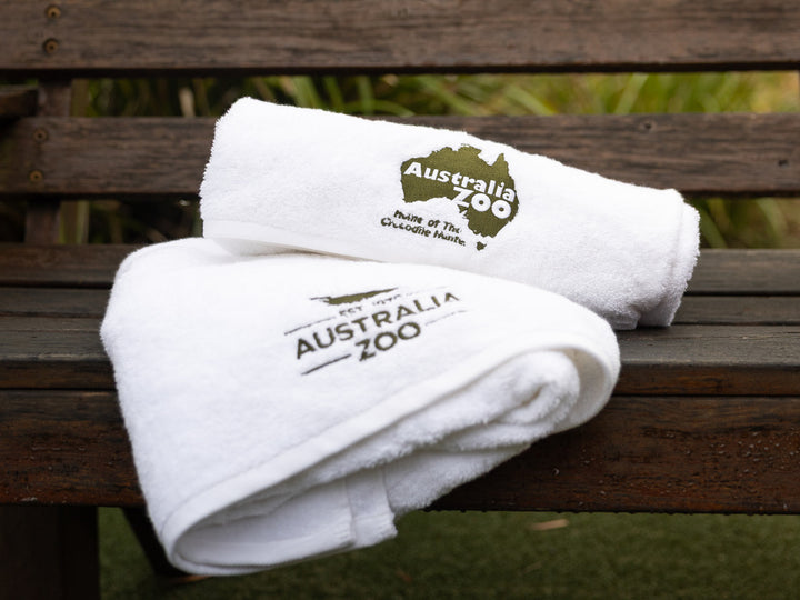 Two white towels with Australia Zoo logo on a wooden bench.