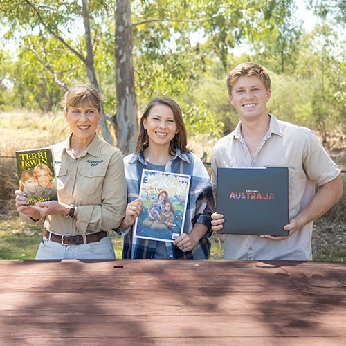 Terri, Bindi and Robert Irwin holding books or albums with a natural outdoor setting
