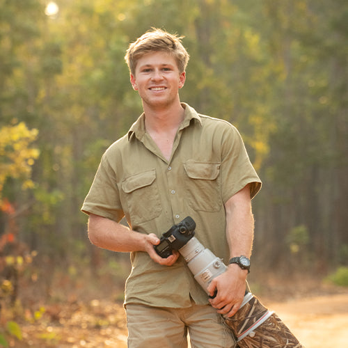 Robert Irwin in a forest holding a camera with a long lens